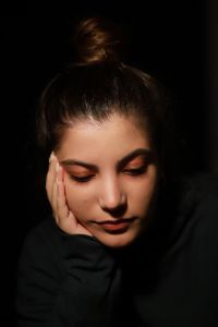 Close-up of young woman against black background