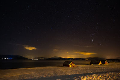 Houses on snow covered lakeshore against star field