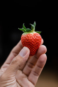 Close-up of hand holding strawberry over black background