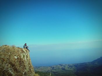 Woman sitting on cliff against sky