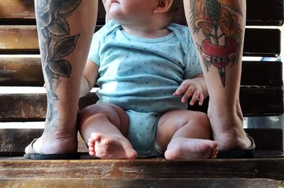 Midsection of a woman with tattoos and baby in between legs