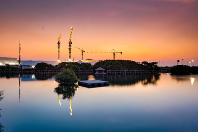 View of factory by lake against sky during sunset