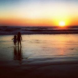 Rear view of friends on beach against sky during sunset