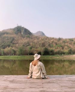 Woman sitting by lake against mountain