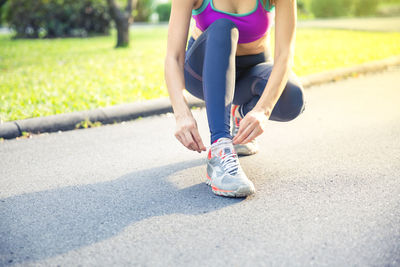 Low section of woman tying shoelace on road