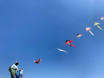 Low angle view of kites flying against clear blue sky