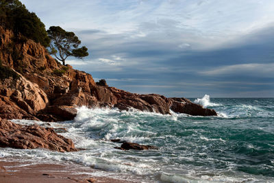 Waves splashing rocks at sea against cloudy sky