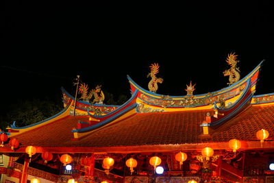 Low angle view of illuminated lanterns by building against sky at night