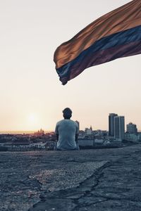 Rear view of man sitting looking at view against clear sky