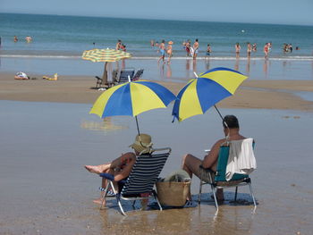 People sitting on chairs at beach against sky