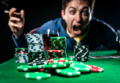 Frustrated man playing poker with whiskey and cigar against black background