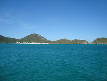 Scenic view of sea and mountains against clear blue sky