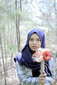 Portrait of woman wearing hijiab holding flowers bouquet at forest