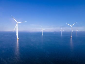 Wind turbines in sea against blue sky