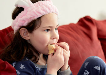 Cute little girl in a pink head dress is eating crepes on the couch