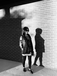 Full length of woman standing against on sidewalk against brick wall