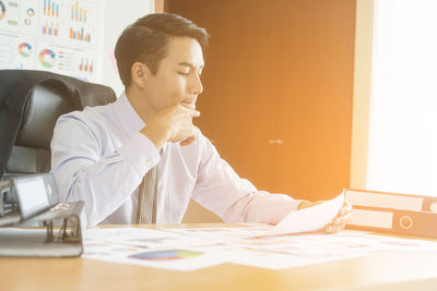 Businessman reading documents while sitting at table in office