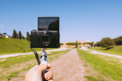 Cropped hand of man taking selfie from camera on monopod against sky