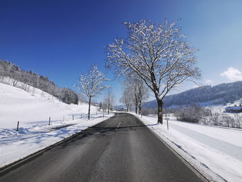 Road amidst snow covered field against blue sky