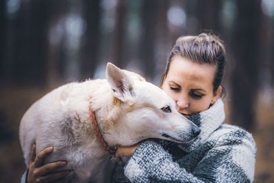 Close-up of woman carrying dog against trees during winter