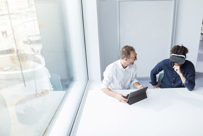 Engineer looking at male colleague examining virtual reality simulator in office