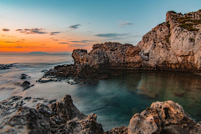 Rock formation on sea shore against sky during sunset