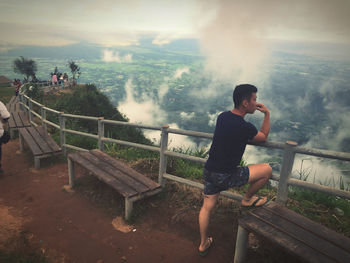 Man standing by railing against mountain and sky during foggy weather