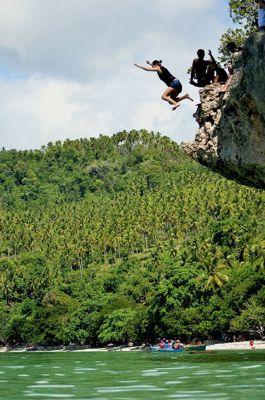 tree, real people, leisure activity, mid-air, lifestyles, men, nature, sky, outdoors, day, water, jumping, cliff, adventure, weekend activities, scenics, beauty in nature, full length, growth, mountain, extreme sports, people