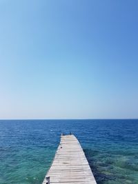 Pier over sea against clear blue sky