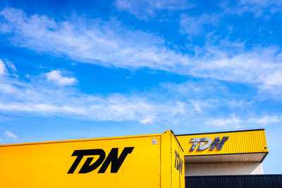 Low angle view of yellow sign against blue sky