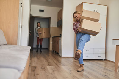 Two young women carrying cardboard boxes into a room