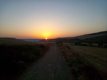 Scenic view of road amidst field against clear sky during sunset