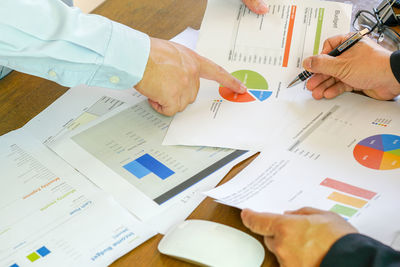 Cropped image of business people discussing over graph at desk in office