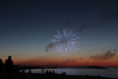 Firework display over sea against sky during sunset