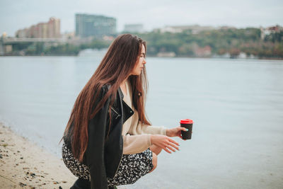 Rear view of young woman photographing while standing against lake