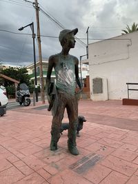 Statue standing by sculpture in city against sky