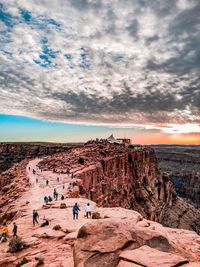 People on rock formations against sky during sunset