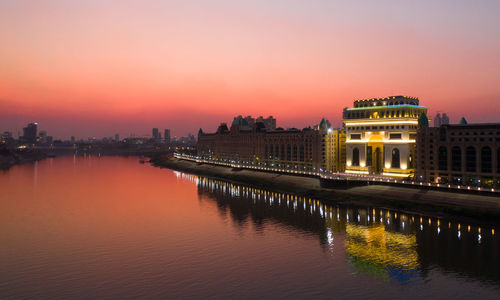 Illuminated buildings at waterfront during sunset