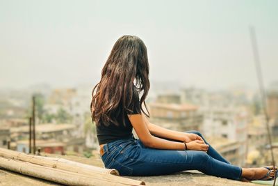 Rear view of woman sitting on railing against sky