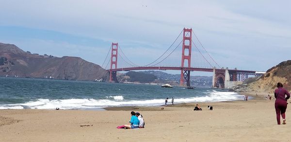 People on beach with suspension bridge in background