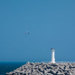 Lighthouse by sea against clear blue sky