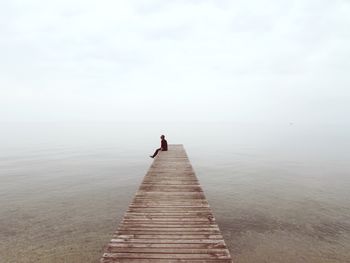 Man sitting on pier against sea at beach