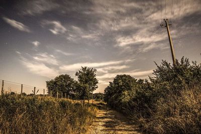 Road passing through field against cloudy sky