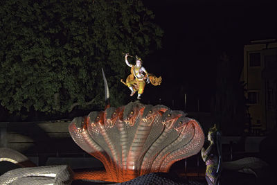 Statue against illuminated trees at night