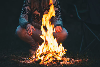 Low section of man crouching by campfire on field at night