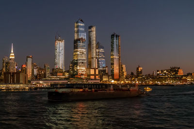 Illuminated modern buildings by sea against clear sky at night