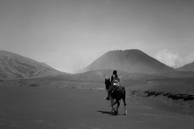 Woman riding horse on sand against mountains