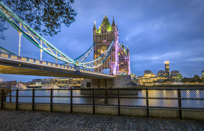 Tower bridge over thames river against cloudy sky in city at dusk