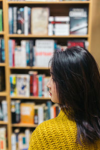 Rear view of woman looking away against shelf