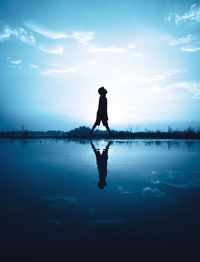 Silhouette boy reflecting on calm lake against sky during sunset